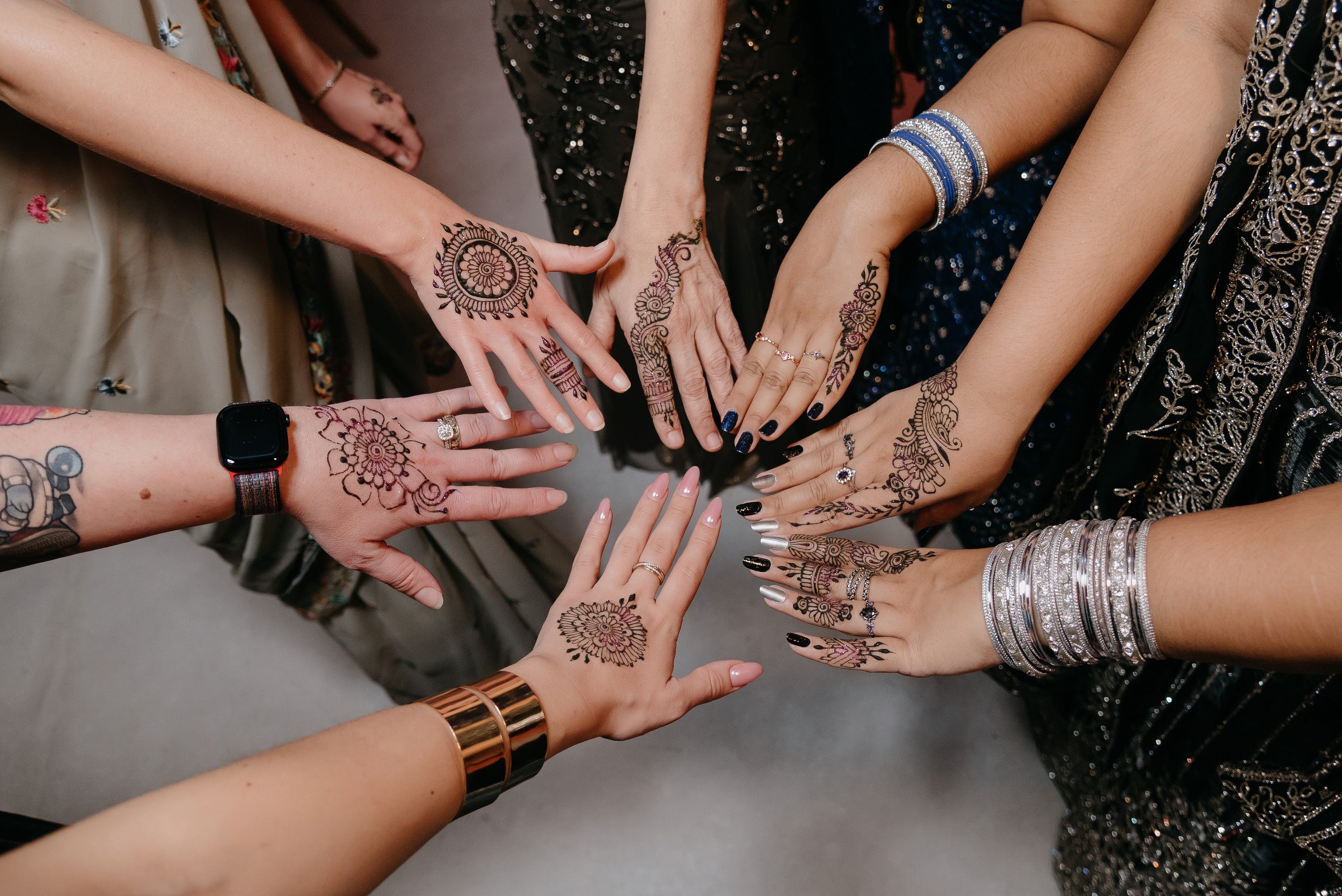 Group of people displaying hands with henna tattoos and silver jewelry.